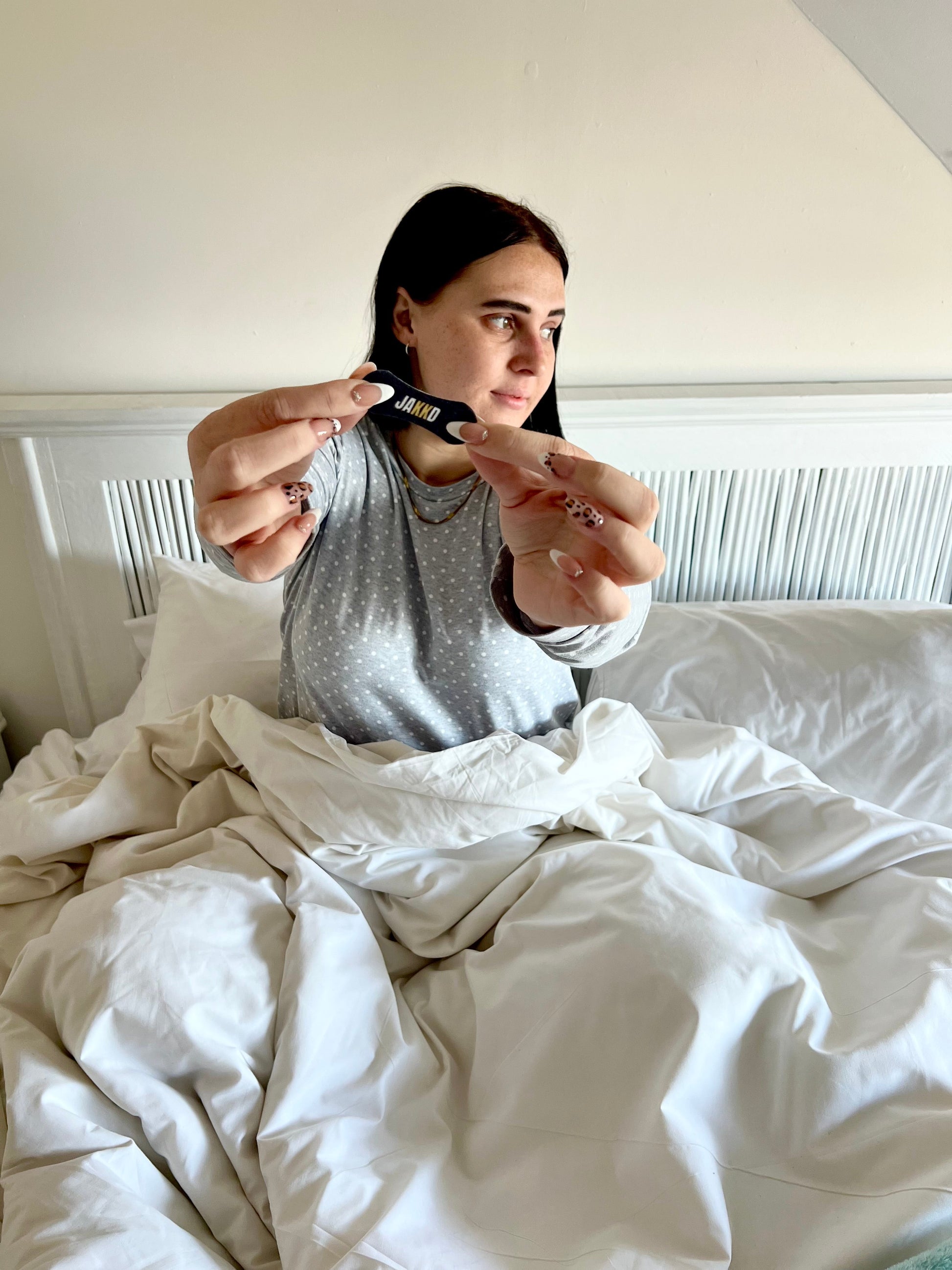 Abigail sitting up in bed holding a single JAKKD nasal strip